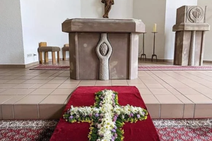 Blumen in Form eines Kreuzes auf rotem Teppich vor einem Altar mit Kruzifix in einer Kirche