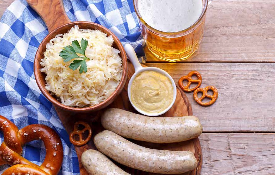 Brett mit drei Weißwürsten, Senf, Sauerkraut in Schale, Brezeln und Bierglas auf Holztisch