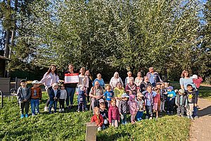 Gruppe von Erwachsenen und Kindern steht auf einer Wiese vor einem großen Baum an einem sonnigen Tag
