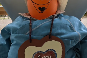 Puppe mit Kürbiskopf, Strohhut und blauem Hemd trägt ein Herzschild mit der Aufschrift 'I mog Di'