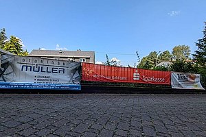 Mehrere Werbebanner mit den Aufschriften 'stahlbau müller', 'Wenn's um Geld geht Sparkasse' und 'UNION' an einem Bauzaun vor einem Gebäude unter blauem Himmel
